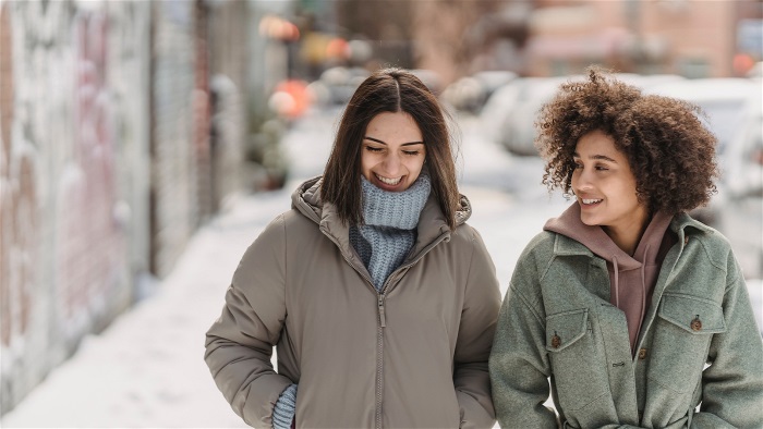 Två unga kvinnor går en promenad i snön och skrattar med varandra.