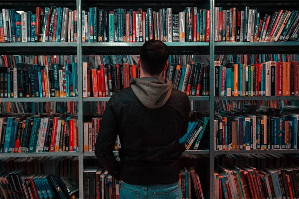 Ett fotografi som visar en person stå framför en bokhylla full av böcker. 