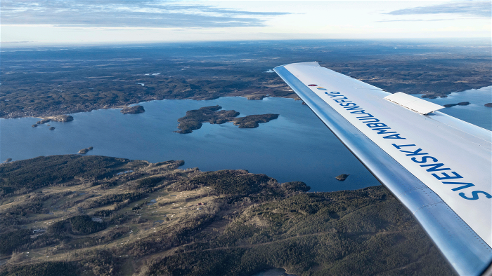 En av vingarna på ett av Svenskt Ambulansflygs flygplan som flyger över ett landskap.