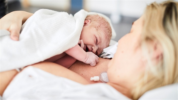 Nyfödd bebis ligger på mammans bröst i sjukhussäng. Foto.