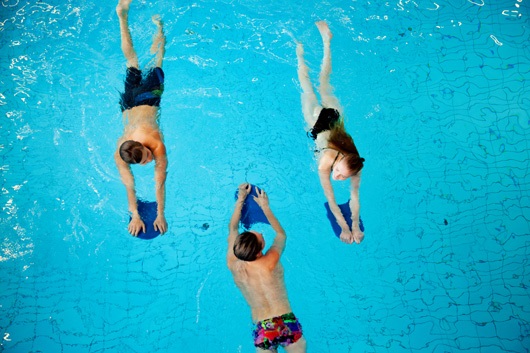 Tre personer simmar i en bassäng