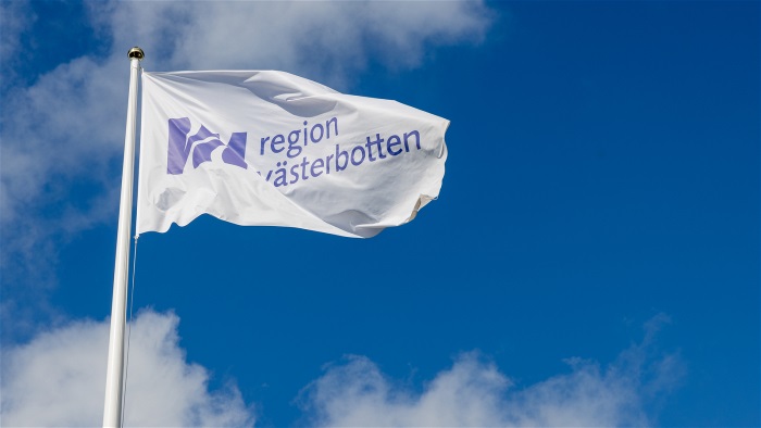 flagga med region västerbottens logotyp mot blå himmel med moln