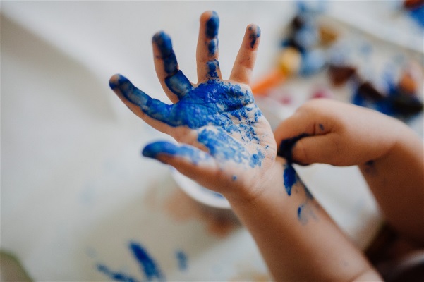 Fotografi av en barnhand täckt av blå färg.