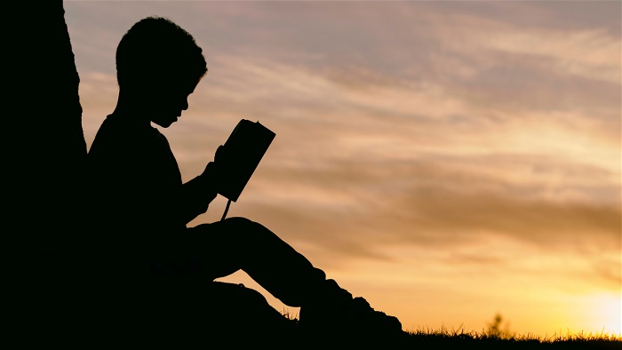 Mörk siluett av ett barn som läser en bok