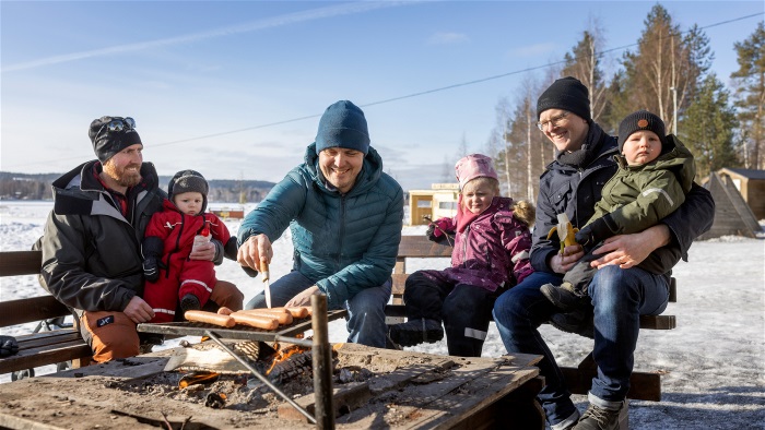 Tre män med små barn grillar utomhus på vintern. Foto.