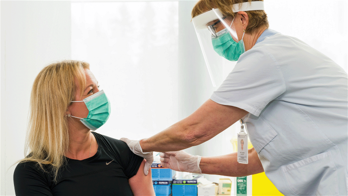 Kvinna vaccineras av sjuksköterska med munskydd och visir.